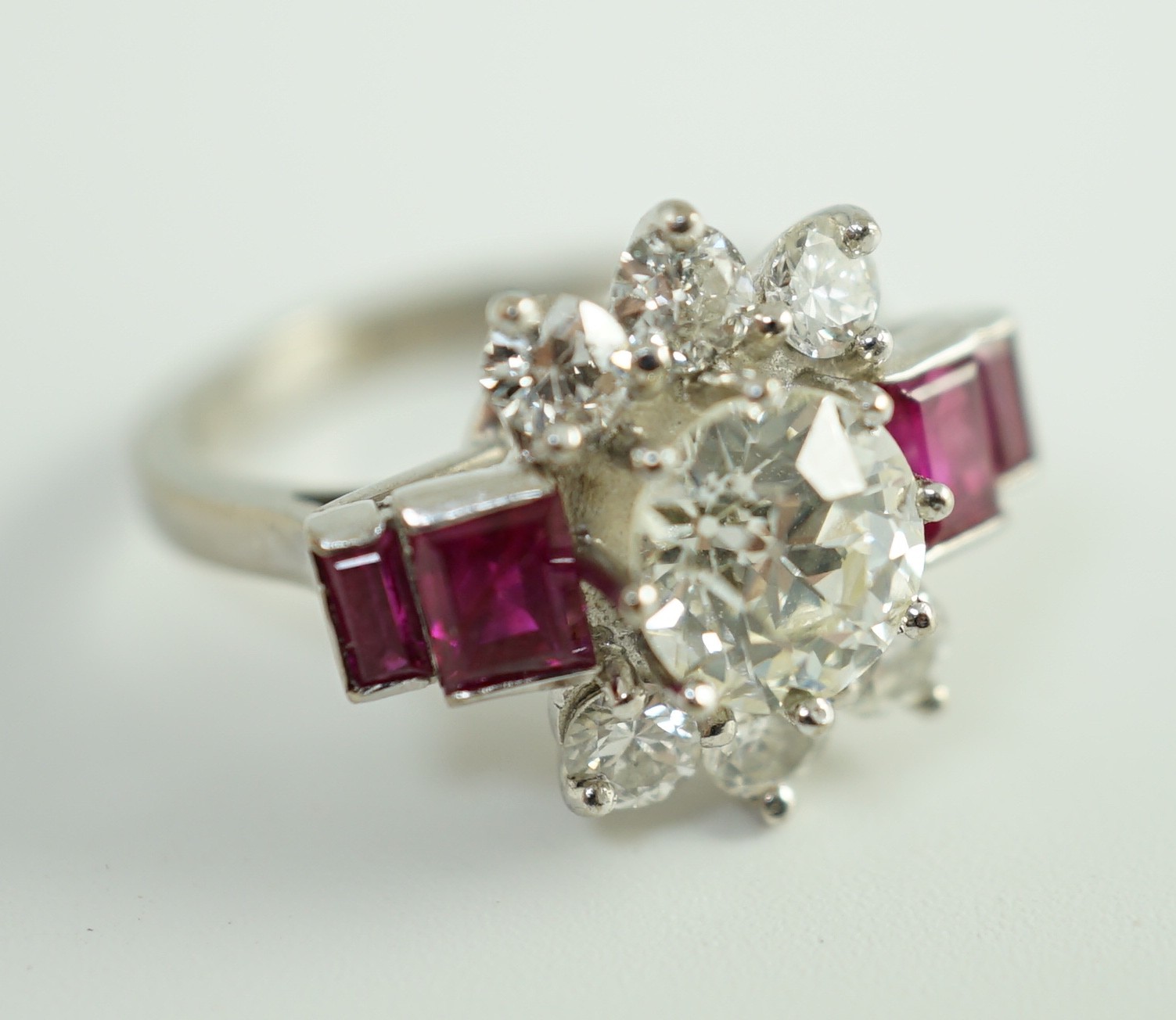 A platinum and single stone diamond dress ring, bordered by six round cut diamond and each shoulder set with two graduated rectangular rubies